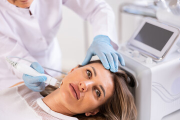 Young female client receiving hardware ultrasonic to revitalize and tighten facial skin at...