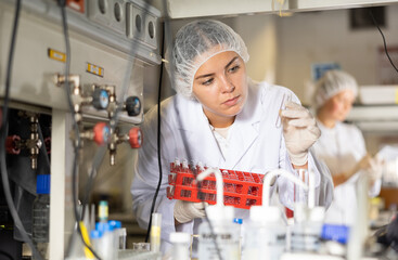 Female pharmacist researcher holding tripod and waiting for color change in test tube while...