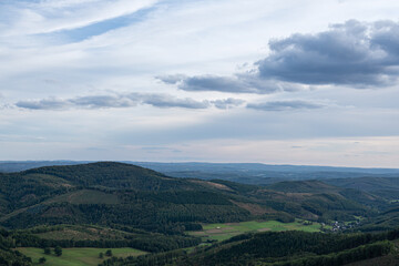 Obraz premium Panoramic view of rolling hills with fields and forests. Countryside landscape under a partly cloudy sky.
