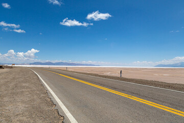 Fototapeta premium Scenic road by the salt flats in Salinas Grandes, Salta, Argentina. Landscape, tourism, travel, trip, desert, adventure, horizon, altitude, blue, sky, remote, destination, nature, wilderness, sky