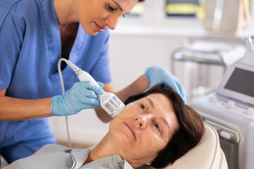 Experienced female cosmetologist performing female face skin massage procedure in cosmetology clinic