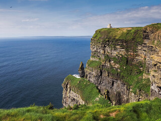 View on Cliff of Moher and O Brien tower. Warm sunny day with cloudy sky and blue ocean water. Famous Irish tourist landmark known for it scenery. County Clare, Ireland.