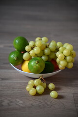 Fresh grapes, limes and lemon in a white bowl on a wooden table. Organic fruits rich in vitamins, perfect for healthy eating, vegetarian diet, and natural food concepts.