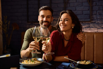 Happy couple toasting with wine in restaurant and looking at camera.