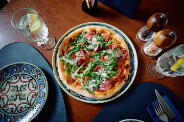 Pizza with prosciutto, mozzarella and fresh arugula in pizzeria.