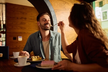 Young happy man being fed by his girlfriend with cake.