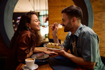 Happy woman being fed with cake by her boyfriend in cafeteria.
