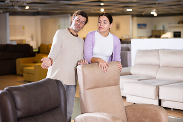 Naklejka premium happy European couple chooses comfortable armchair in furniture store