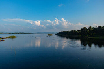 Kaptai Lake shore with vibrant fishing boats, lush greenery, and clear reflections of clouds in the water.