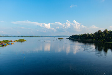 Tranquil Kaptai Lake view featuring a green forested shore, scattered water plants, and serene blue skies.