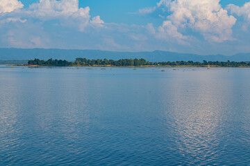 Wide-angle view of tranquil Kaptai Lake surrounded by greenery with floating vegetation and peaceful water.