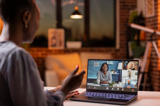 Black female entrepreneur working indoors, attending virtual business meeting with clients and coworkers. Professional woman speaking on video call with shareholders from cozy apartment desk.