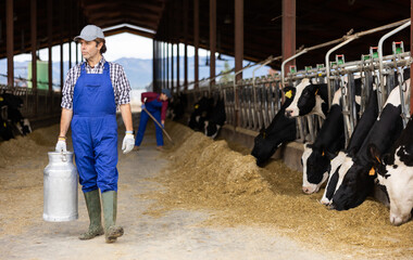Dairy farmer man carrying aluminum can of milk in cowshed