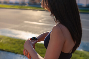 Young woman checking smartwatch during outdoor exercise in a urban setting, focusing on health and...