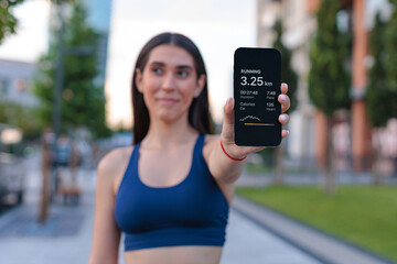 Female runner shows distance and calories burned on smartphone during outdoor workout in urban setting