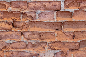 A close-up photograph of a weathered clay brick wall. The crumbling surface and imperfections of...