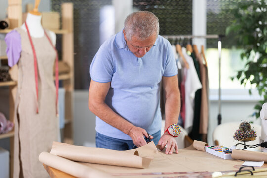 Mature man cutting paper in sewing workshop. Tailor makes patterns for clothes