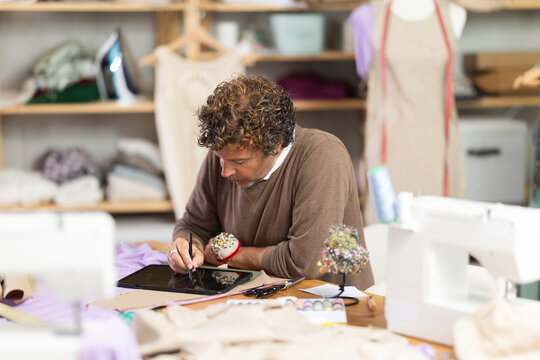 Qualified fashion designer draws a fashion design with a size grid on an electronic tablet. Tailor works in a sewing workshop - Powered by Adobe
