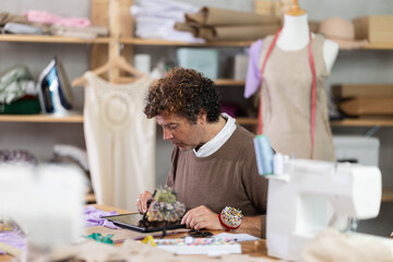 Adult male tailor draws pattern using tablet in sewing workshop