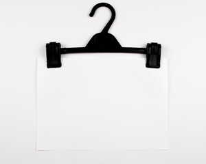 Black hanger with white paper sheet on white background with copy space