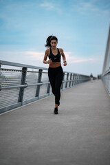 Naklejka premium Young sporty woman running on a bridge in the city