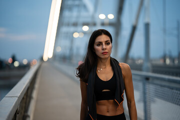 Sporty woman walking on bridge after workout at dusk