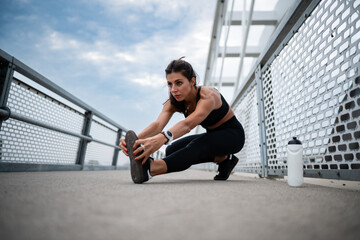 Sporty woman stretching legs on bridge before running
