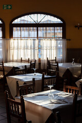 Sunlight filtering through windows of a traditional restaurant interior with empty tables and chairs. Gibraltar, Spain. September 2025.