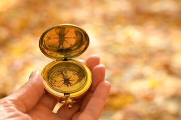 Woman’s hand holding golden compass with blurred autumn nature background © Julia