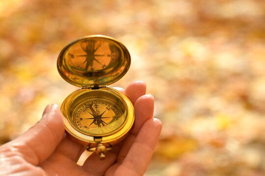 Woman’s hand holding golden compass with blurred autumn nature background