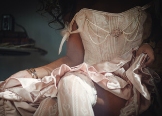 Woman in pink retro dress with corset, lace stockings and pearl-like beads