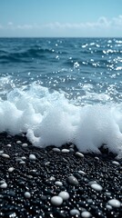 Foamy waves crashing on black pebble beach with shimmering ocean backdrop.