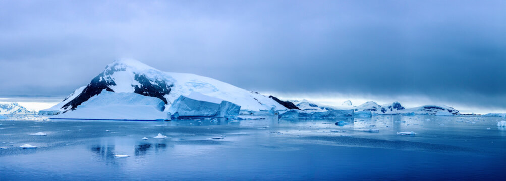 Panoramic view of the Antarctic landscape with snow-covered mountains, floating icebergs, and calm polar waters