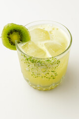 A refreshing and vibrant yellow cocktail with ice cubes, garnished with a slice of kiwi and a rim of sugar and lime zest, served in a glass on a bright white background.