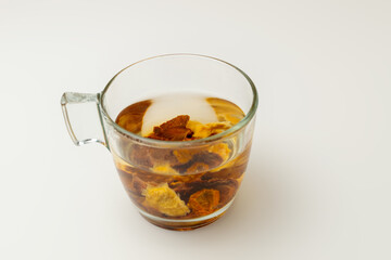 A close-up of a clear glass mug with natural fruit or vegetable pieces and water, creating a warm, healthy infusion, on a clean white background, ideal for recipes, and natural product promotions.