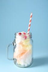 Colorful cotton candy and straw in mason jar on light blue background, closeup