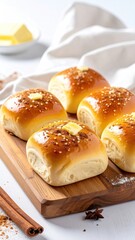 Freshly baked dinner rolls, golden-brown, glazed, and buttered, sit on a light-brown wooden board