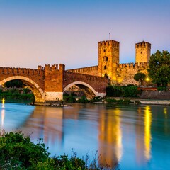 Fototapeta premium Ancient stone bridge over a river, with castle walls and towers. Twilight hues