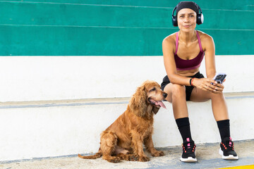 latin senior woman, 48 years old, sitting on stadiumgrandstands with her cocker spaniel dog,...