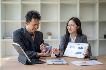 Asian businesspeople discussing and analyzing financial charts using mobile phone and documents at office desk
