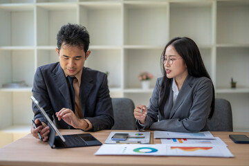 Business colleagues discussing financial charts and data on tablet and laptop in office meeting