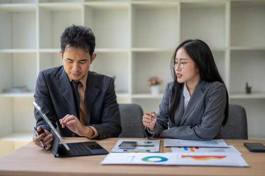 Business colleagues discussing financial charts and data on tablet and laptop in office meeting - Powered by Adobe