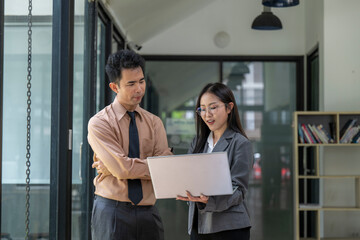 Business colleagues discussing work using laptop in office hallway