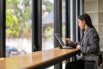 Businesswoman working on tablet with stylus in modern office by window