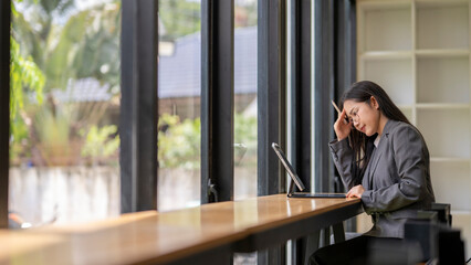 Stressed businesswoman having headache while working on tablet in office