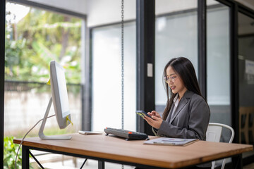 Businesswoman using smartphone and computer in modern office