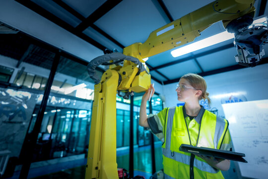 A female automation engineer oversees the operation of a 6-axis industrial robotic arm in a smart factory, representing human oversight in a complex Industry 4.0 environment.