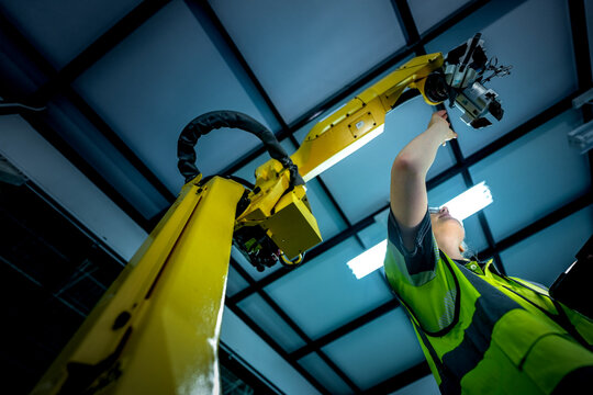 A female maintenance technician performs a preventative maintenance check on a 6-axis robotic arm's end-effector, ensuring the system's precision on the production line.