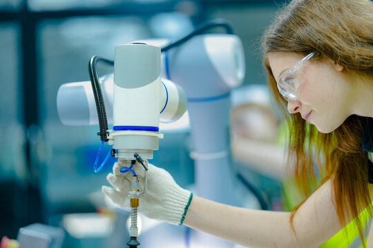A female technician attaches a pneumatic end-effector to a 6-axis collaborative robot (cobot). She is setting up the robotic cell for a precise, automated assembly task.