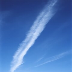 A wispy, white, high-altitude cloud streak against a vibrant blue sky